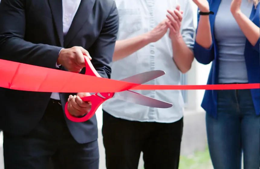 a group of people with large scissors cutting a red ribbon