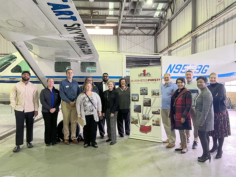 partners doing a business walk and photo with an air plane behind them and a BusinessFirst! banner